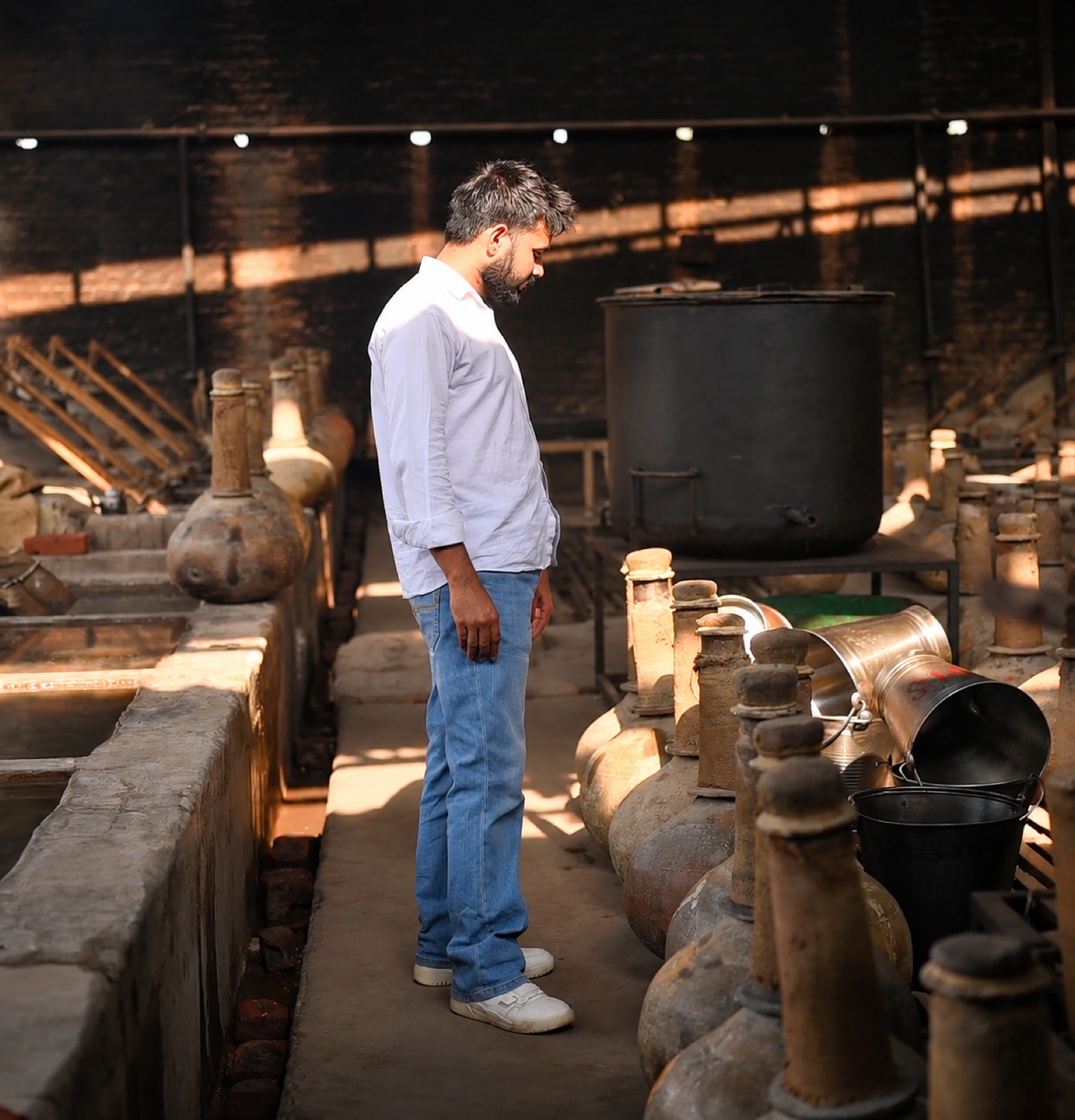Sunlight across traditional distillation vessels in a Kannauj perfumery workshop